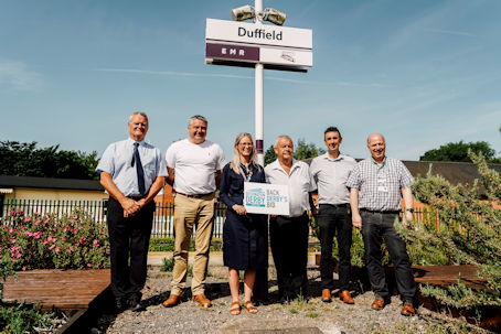 Derwent Valley Line Community Rail Partnership holding a 'Back Derby's Bid' sign at Duffield train station
